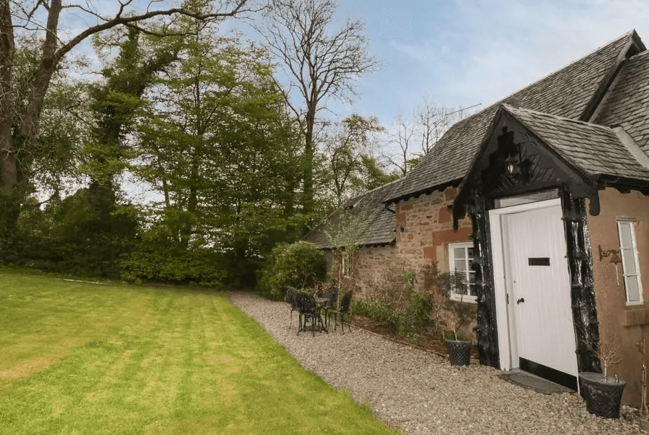 Traditional stone cottage with dark wood porch and mature garden at Ellanderroch, Drymen