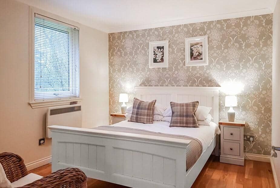 Bedroom with white wooden bed frame and patterned wallpaper at Leven Lodge 3