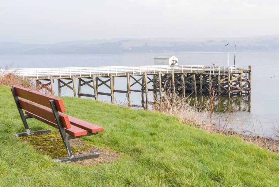 Red bench on the grassy bank with views of the wooden pier extending into the loch at Pier View
