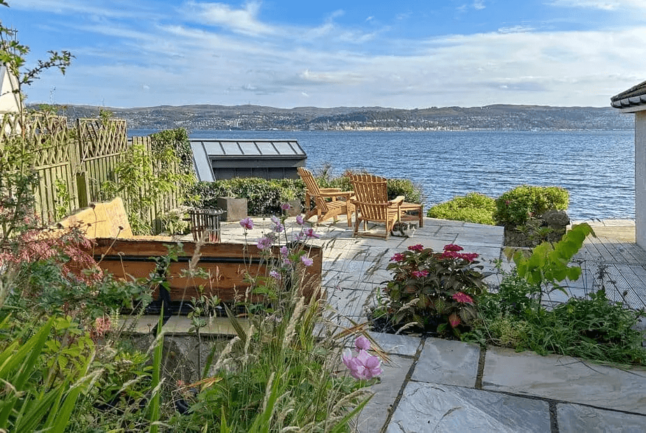 Outdoor lounge chairs on the stone terrace with sea views and garden plants at Shore House