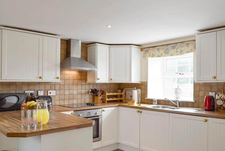 Country kitchen with white cabinetry and warm wooden countertops at The Stables